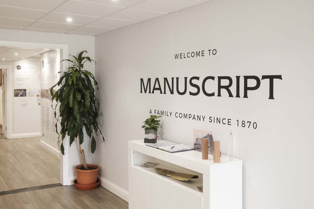 An image of the hallway, on the wall it says "welcome to manuscript a family company since 1970"
